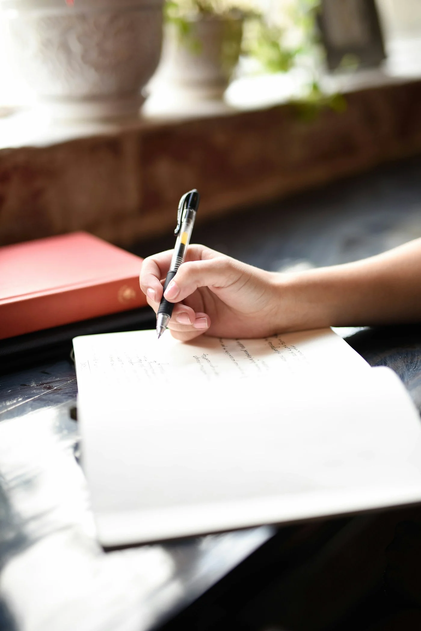 A person writing by hand in an open notebook beside a softly lit window.