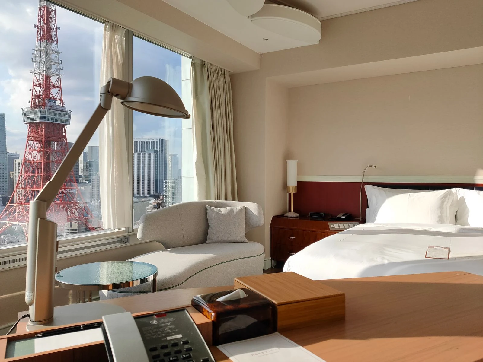 A warm-toned Tokyo hotel room with cream seating, a bed and a view of Tokyo Tower.