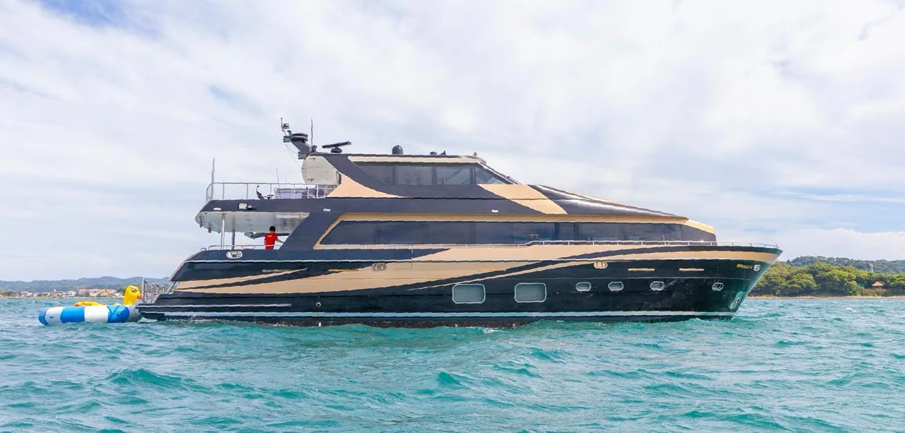 Dark-hulled yacht with gold trim on turquoise water.